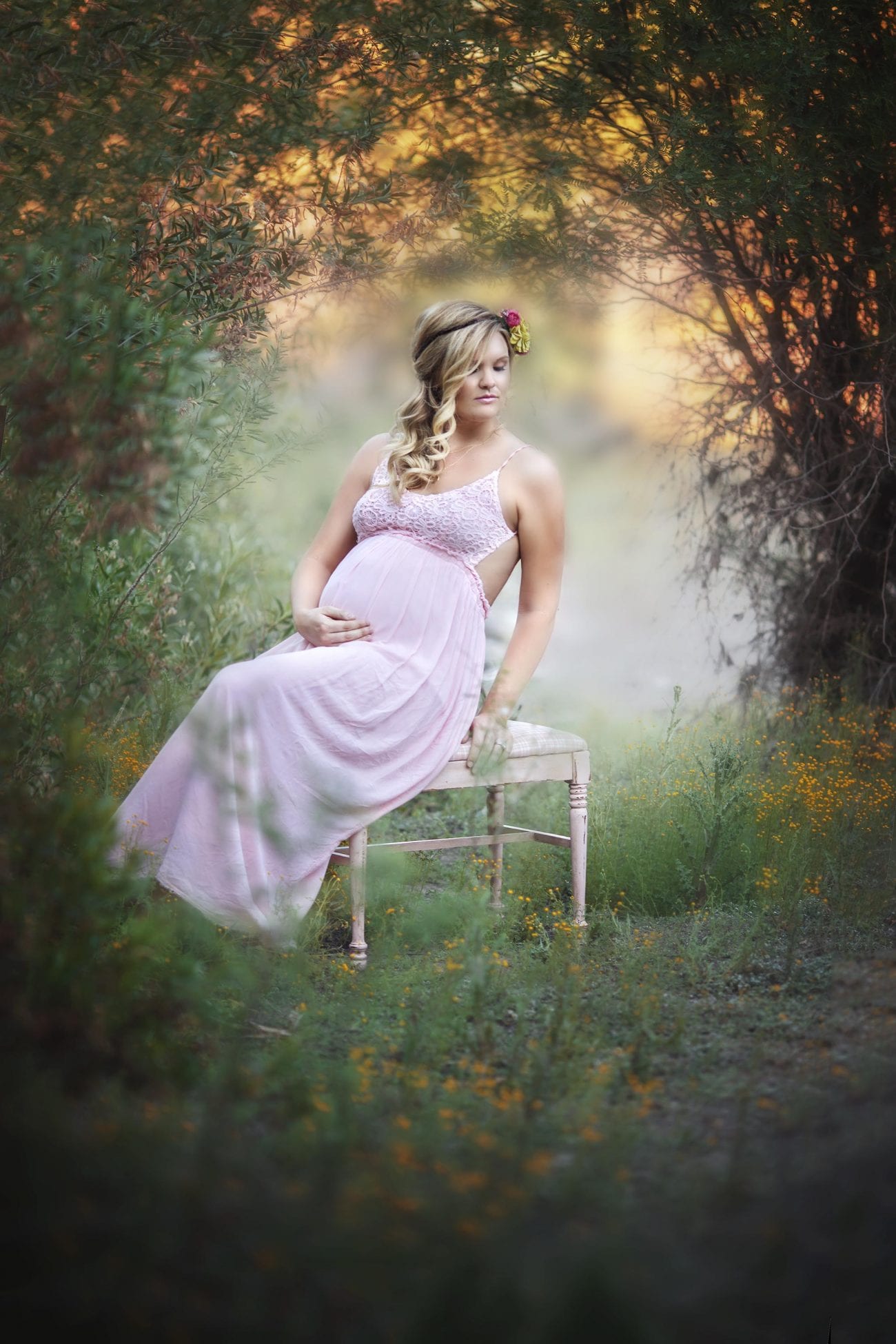 Maternity photography near downtown Phoenix in green grassy field location. Model is wearing a flower crown and flowing pink maternity gown