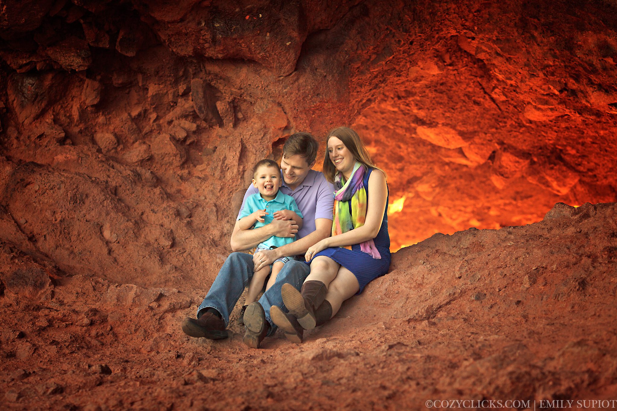 Family of three sitting at the Hole in the Rock.  backlground is red and looks like it is on fire with the setting sun