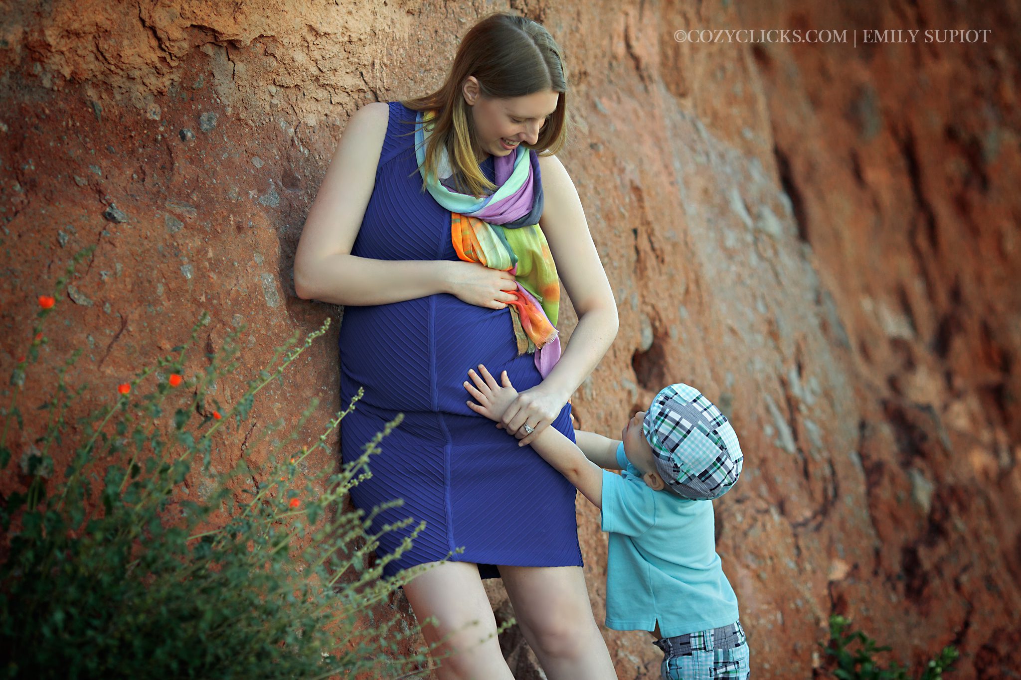 Family maternity photo with mom and her two year old son reaching up to touch mom's belly