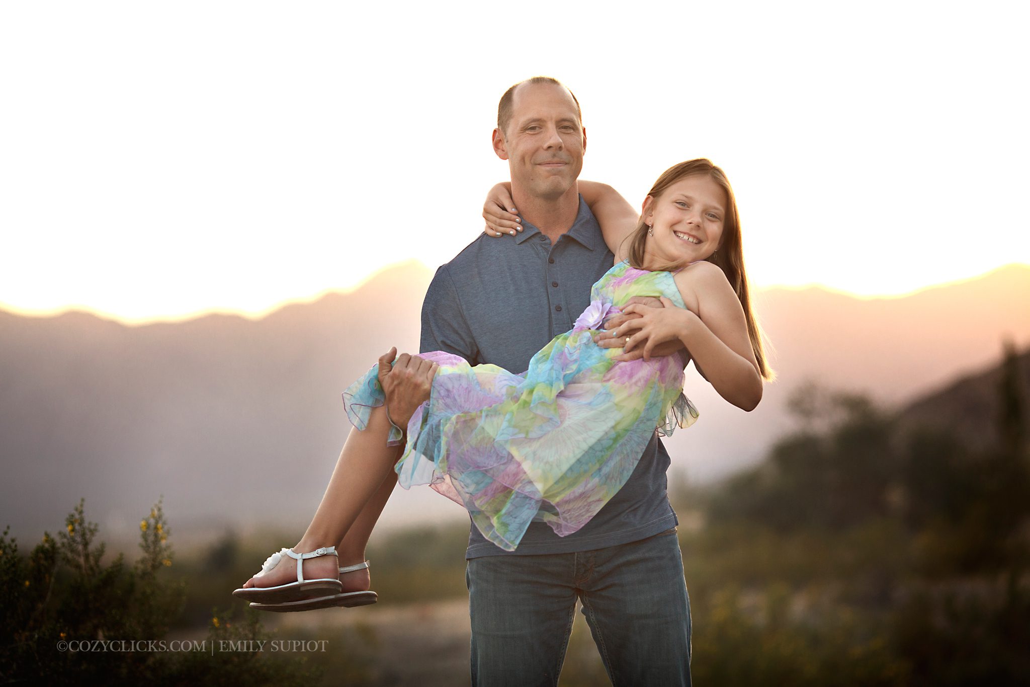 Father and daughter pose together near the mountain trail at sunset