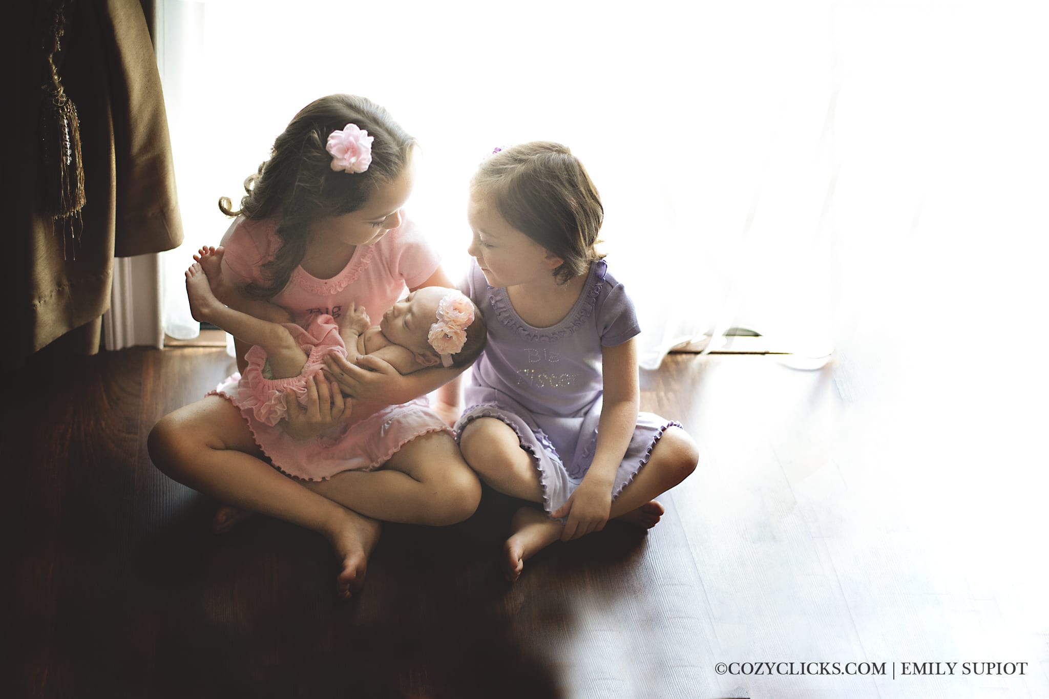 Three sisters.  Older sisiters holder their newboorn baby girl in this adorable newborn family shot