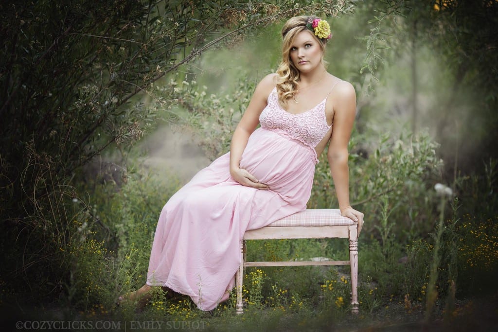 Full body maternity picture of pregnant woman sitting in a filed of flowers and green grass