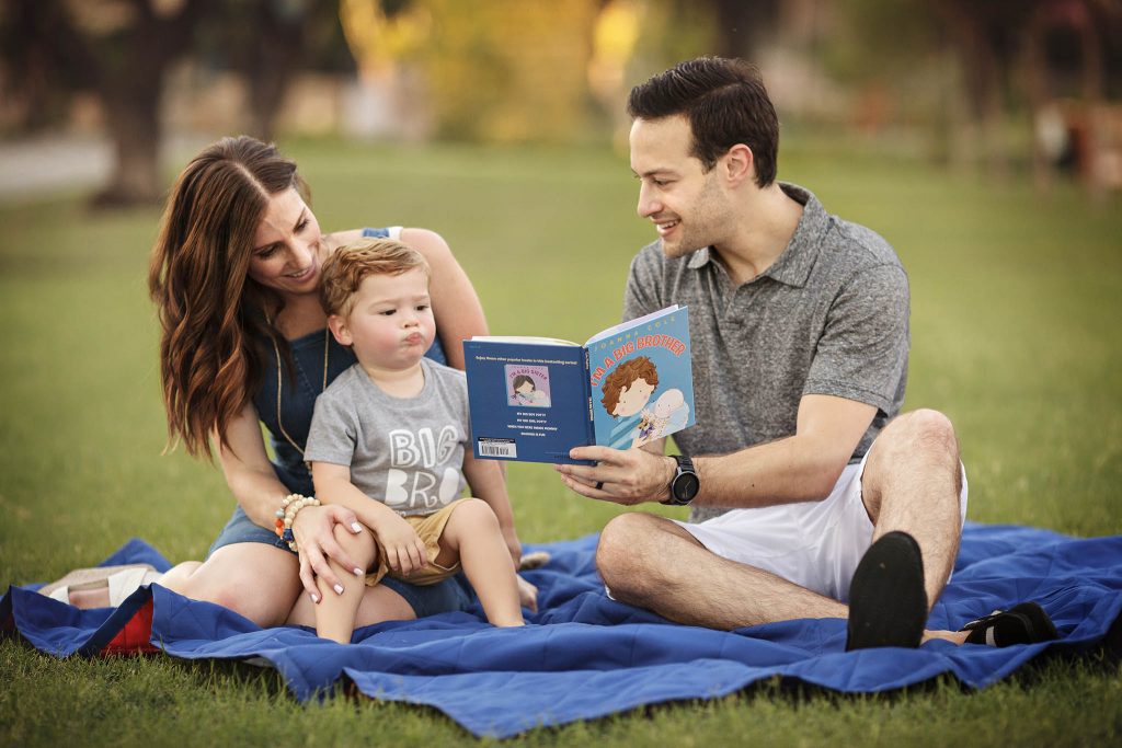 Pregnancy announcement photo with family of three reading an I'm a Big Brother Book