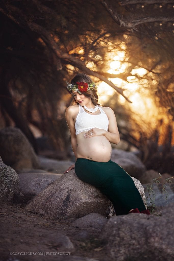 Maternity photography at Coons Bluff. Mom to be on a rock loooking down at her belly wearing a flower crown