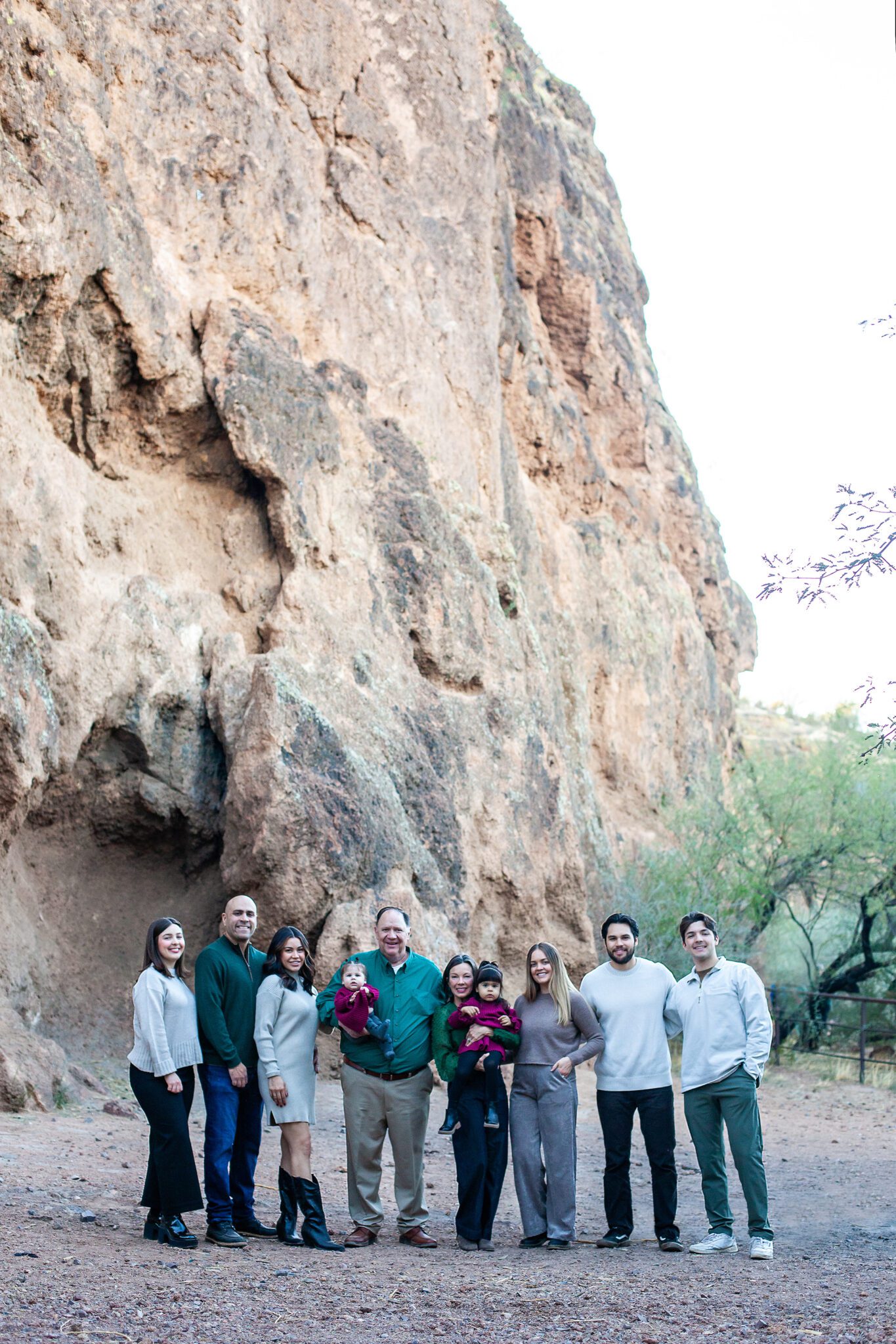 Large family dressed in coordinating neutral tones, smiling and laughing under the towering trees at Coon Bluff."